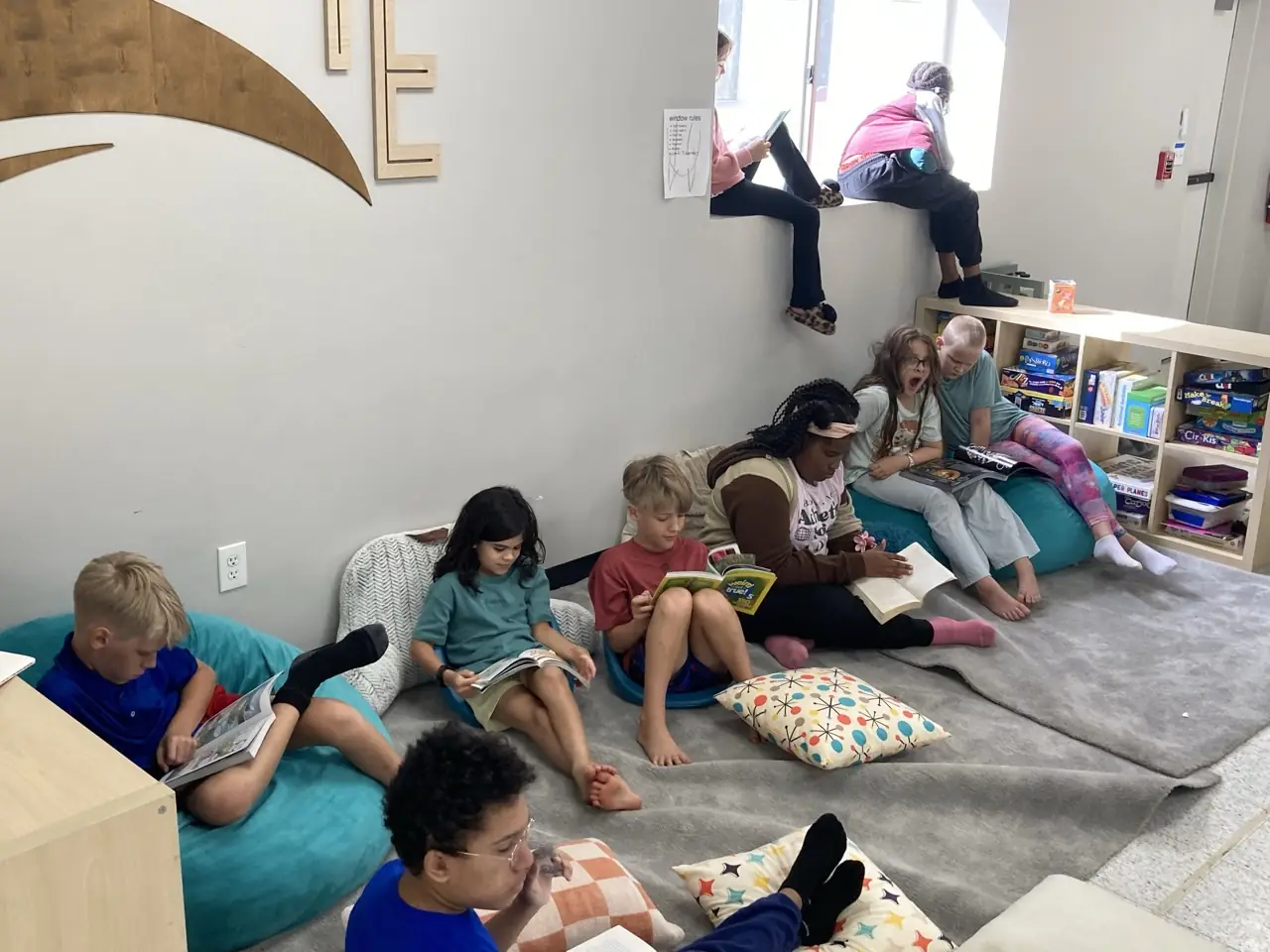 Learners read on bean bags, a window seat, and the floor beside bookshelves.