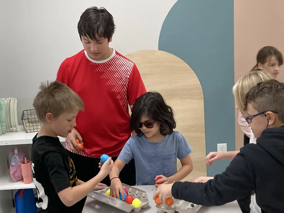 Learners stand around a table sorting brightly colored eggs into cartons.